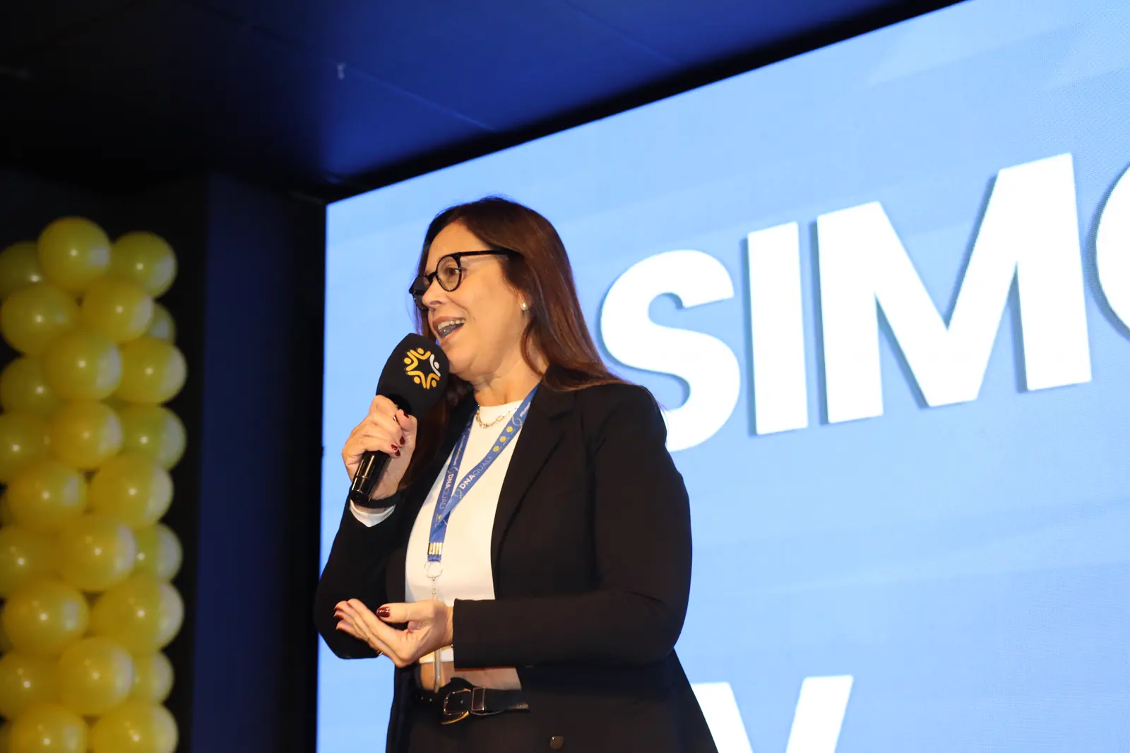 Palestrante falando ao microfone diante do telão azul do Centro de Convenções